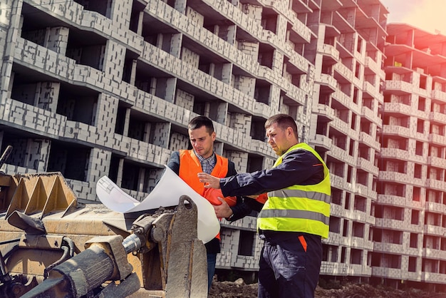 Due operai in tuta ed elmetto stanno vicino al nuovo edificio e parlano