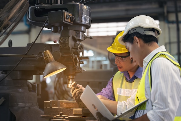 Due operai nello stabilimento di produzione come squadra che discute, scena industriale in background, che lavorano insieme alle attività di produzione