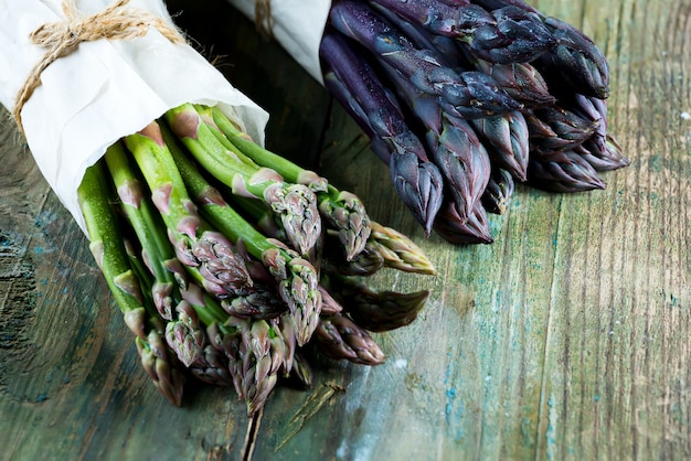 Due pacchi organici naturali freschi di verdure verdi e porpora dell'asparago su un fondo di legno.