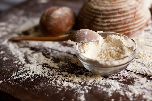 Due pagnotte di pane gustoso appena sfornato ciotola di farina e cucchiaio di legno sono sul tavolo marrone