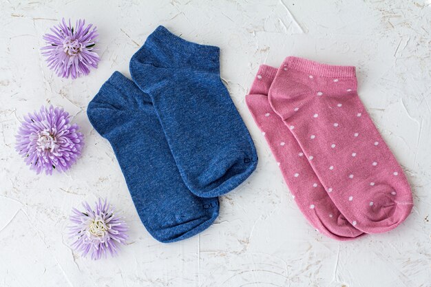 Due paia di calzini da donna blu e rosa con fiori di aster sullo sfondo bianco strutturato, vista dall'alto.