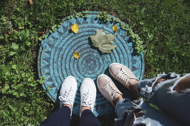 Due paia di gambe di donne e foglie cadute sul tombino