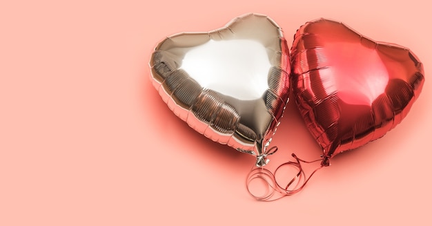 Due palloncini stagnola a forma di cuore su uno sfondo rosa con posto per il testo. Palloncini rossi e argento su sfondo chiaro.