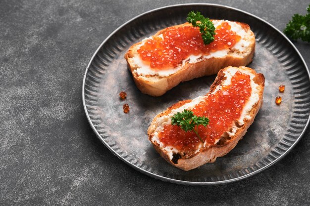 Due panini con caviale rosso Caviale rosso salmone in ciotola e server per sandwich su vecchia piastra di ferro su vecchio sfondo nero tavolo Vista dall'alto Spazio di copia