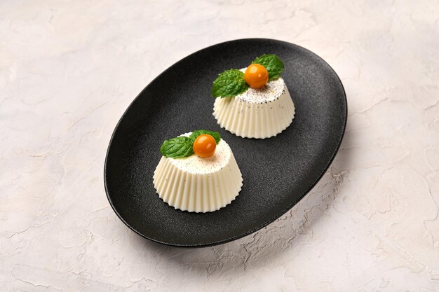 Due panna cotta fatta in casa con baccello di vaniglia naturale physalis o ciliegia invernale e menta su ovale nero