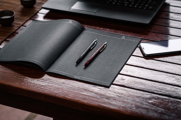 Due penne ufficio che giace su un taccuino nero vicino a un telefono e un computer portatile