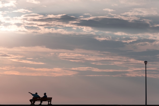 Due persone sedute su una panchina di strada e guardando il bellissimo tramonto drammatico