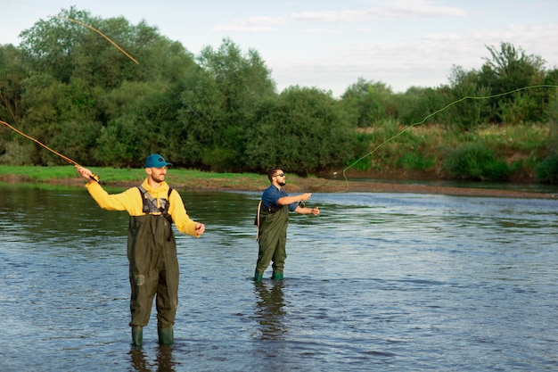 Due pescatori sono in piedi nel fiume con stivali di gomma