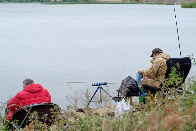 Due pescatori sono seduti su sedie durante una battuta di pesca sulla riva di un lago artificiale