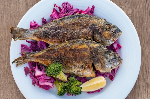 Due pesci di mare alla griglia serviti su un piatto con cavolo rosso broccoli verdi e limone Primo piano