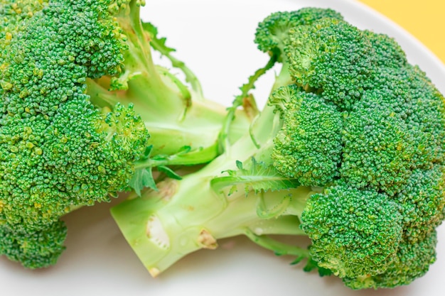 Due pezzi di broccoli freschi e crudi su piatto bianco Cavolo verde crudo