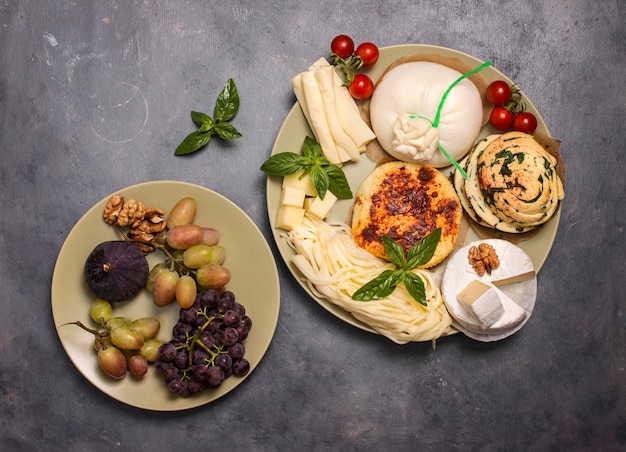 Due piatti con formaggio e noci d'uva e fico su sfondo grigio