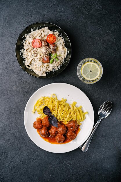 Due piatti di pasta con polpette di carne vegetale funghi basilico pomodoro e salsa di panna pomodori su uno sfondo di cemento scuro spazio copia vista dall'alto