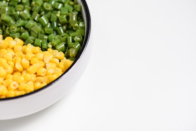 Due piatti di verdure a colori: fagiolo verde tagliato a cubetti e kernel di mais giallo, su sfondo bianco con spazio negativo.