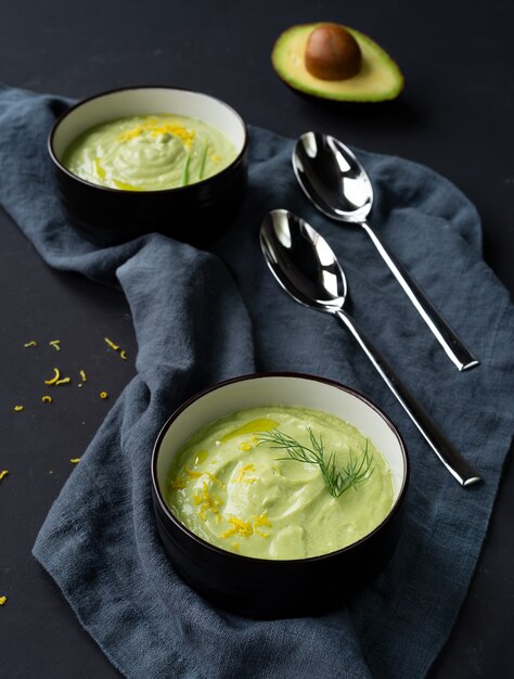 Due piatti scuri con crema di zuppa di cetrioli e avocado con scorza di limone e olio d'oliva su sfondo nero. Vista dall'alto. orientamento verticale.