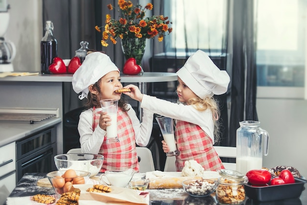 Due piccole bambine felici che bevono latte e cucinano al tavolo in cucina sono adorabili e belle