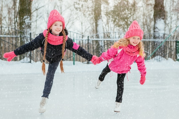 Due piccole ragazze sorridenti che pattinano sul ghiaccio nell&#39;usura rosa e nelle sciarpe fatte a mano.