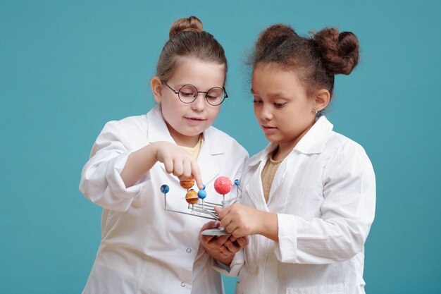 Due piccoli chimici in camice bianco che esaminano insieme la formula chimica sullo sfondo blu