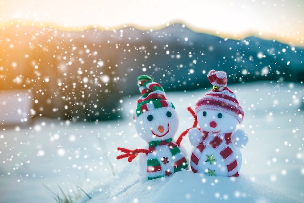 Due piccoli giocattoli divertenti bambino pupazzo di neve in cappelli lavorati a maglia e sciarpe nella neve profonda all'aperto su montagne sfocate sullo sfondo del paesaggio. Tema della cartolina d'auguri di felice anno nuovo e buon Natale.