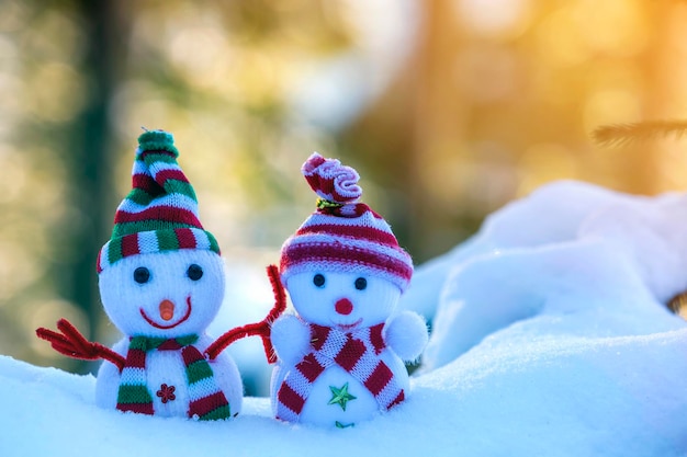 Due piccoli giocattoli divertenti bambino pupazzo di neve in cappelli lavorati a maglia e sciarpe nella neve profonda all'aperto su sfondo luminoso blu e bianco copia spazio Felice anno nuovo e buon Natale biglietto di auguri