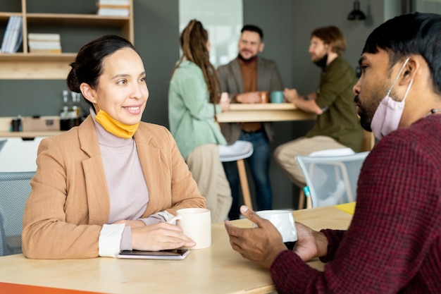 Due piccoli gruppi di giovani designer o manager interculturali che prendono un caffè e discutono di piani di lavoro o idee creative durante una pausa