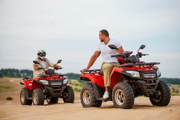 Due piloti atv che corrono nelle sabbie del deserto. Persone di sesso maschile su quad, gara di sabbia, safari sulle dune in una calda giornata di sole, avventura estrema 4x4, concetto di quad-bike