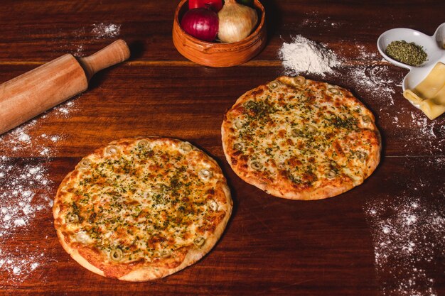 Due pizze personali accanto agli ingredienti su un tavolo di legno.