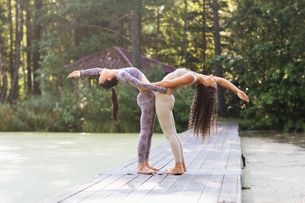 Due praticanti di yoga femminili che si tengono l'un l'altro facendo la posa di Hasta Uttanasana backbend