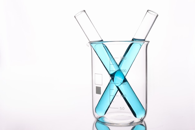 Due provette con acido blu in piedi in un bicchiere di vetro su parete bianca