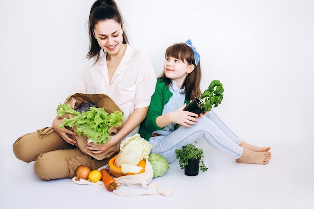 Due ragazza disimballaggio shopping eco bag con verdure, verdi senza plastica su sfondo bianco. Zero sprechi, senza plastica Concetto ecologico.