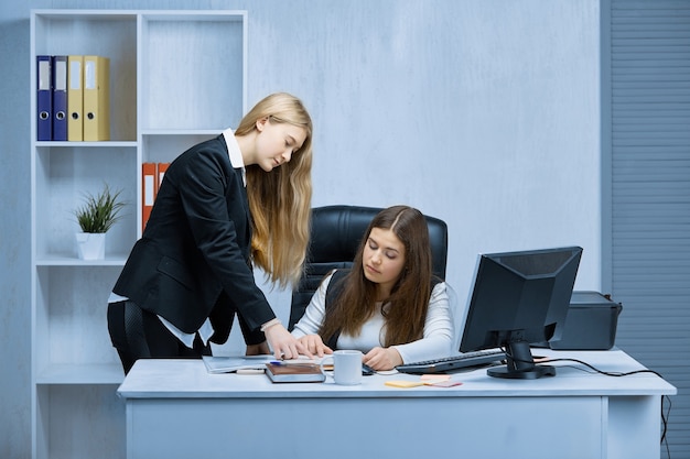 Due ragazze a una scrivania bianca in ufficio si consultano durante l'esame di un progetto comune