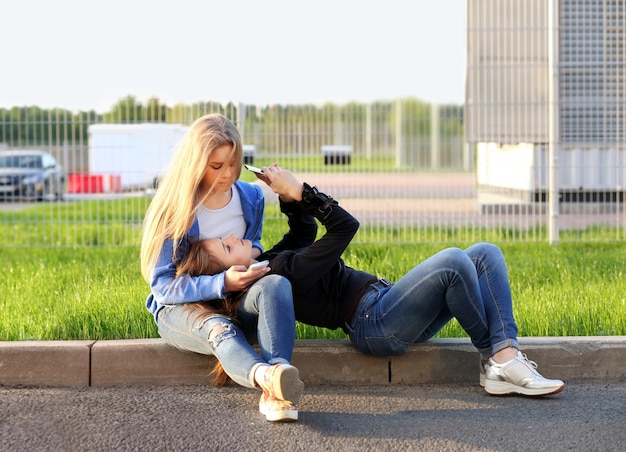 Due ragazze adolescenti che usano lo smartphone prendendo un selfie seduti insieme Due ragazze che ridono e fanno smorfie