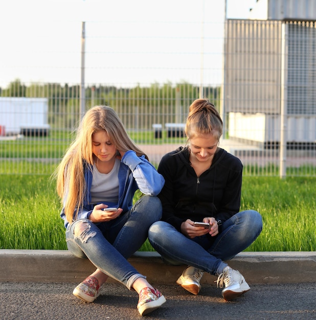 Due ragazze adolescenti che usano lo smartphone prendendo un selfie seduti insieme Due ragazze che ridono e fanno smorfie