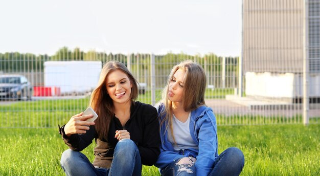 Due ragazze adolescenti che usano lo smartphone si fanno un selfie seduti insieme Due ragazze che ridono e fanno smorfie