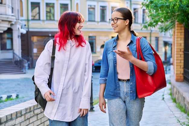 Due ragazze adolescenti ridenti che parlano a piedi camminando per la strada della città