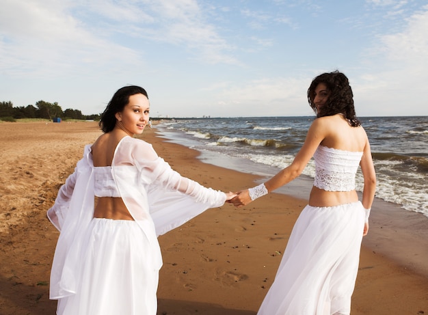 Due ragazze adorabili che indossano camminata bianca sulla spiaggia