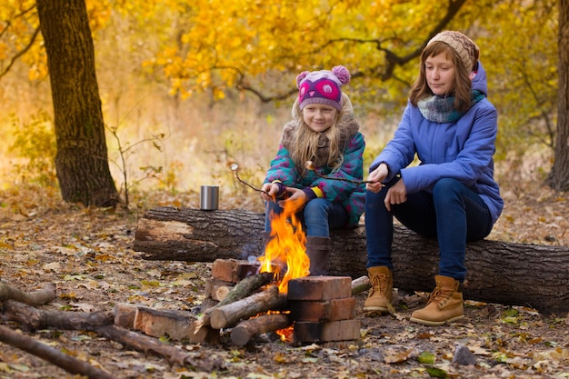 Due ragazze al picnic nella foresta autunnale sedute intorno al falò