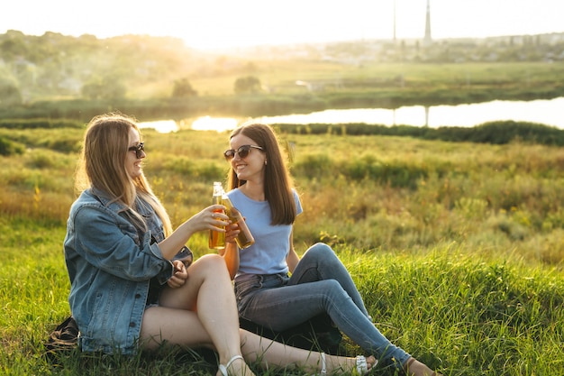 Due ragazze allegre e giovani amici con gli occhiali da sole, bevendo birra e godendosi il tempo trascorso insieme al tramonto.