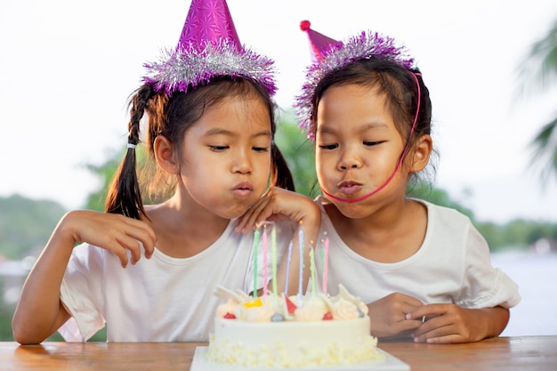 Due ragazze asiatiche bambino festeggia il compleanno e soffiando le candeline sulla torta di compleanno nella festa