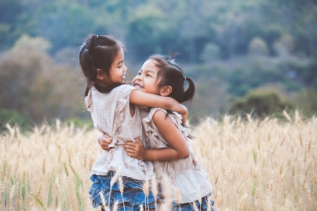 Due ragazze asiatiche che si abbracciano con amore e giocano insieme nel campo di orzo