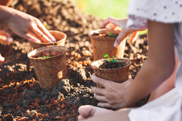 Due ragazze asiatiche del bambino che piantano le giovani piantine dentro riciclano insieme i vasi di fibra nel giardino