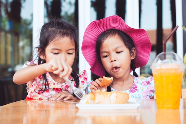 Due ragazze asiatiche del piccolo bambino sveglio che mangiano pane tostato e succo d&#39;arancia deliziosi