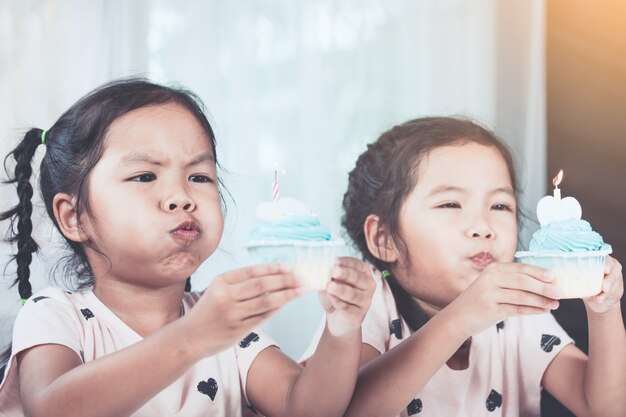 Due ragazze asiatiche sveglie del bambino divertendosi a soffiare insieme il cupcake di compleanno nel tono di colore d&#39;annata