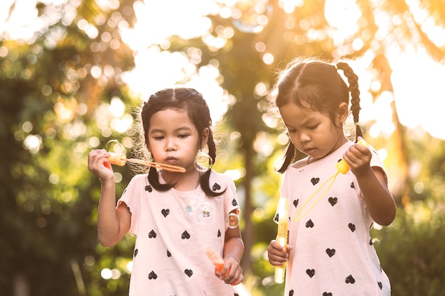 Due ragazze asiatiche sveglie del bambino divertendosi da giocare insieme con le bolle in all&#39;aperto al tramonto