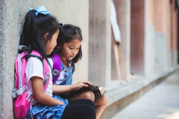 Due ragazze asiatiche sveglie dell&#39;allievo che leggono insieme un libro nella scuola con divertimento e felicità