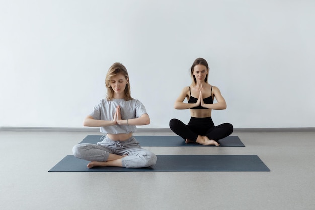 Due ragazze atletiche e attraenti si siedono nella posizione del loto su un tappetino da yoga al chiuso Yoga fitness e stile di vita sano