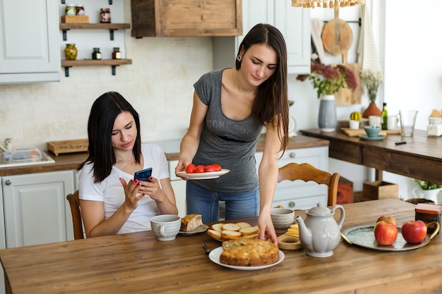 Due ragazze brune stanno bevendo il tè con torta e dolci al tavolo.