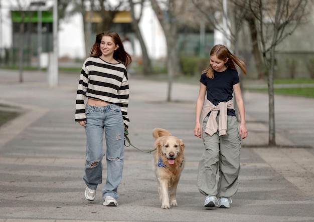 Due ragazze camminano con un cane golden retriever lungo un vicolo in primavera