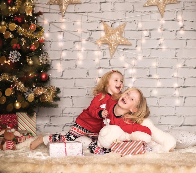 Due ragazze carine allegre in abiti natalizi sullo sfondo dell'albero di Natale