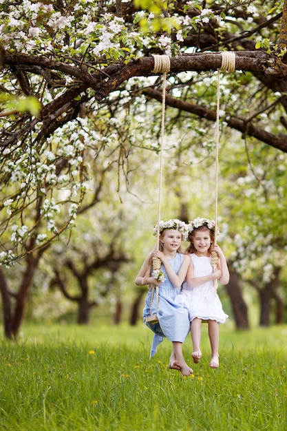 Due ragazze carine che si divertono su un'altalena nel giardino di un vecchio albero di mele in fiore Giornata di sole Attività all'aperto primaverili per bambini